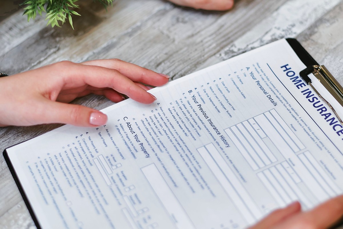 Two people's hands go over home insurance paperwork on a clipboard at a wooden table.