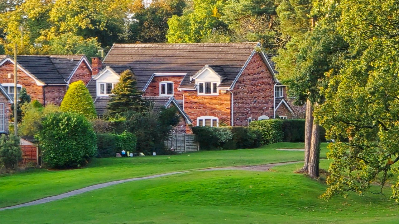 A rolling green lawn below red brick houses and trees just starting to turn gold.